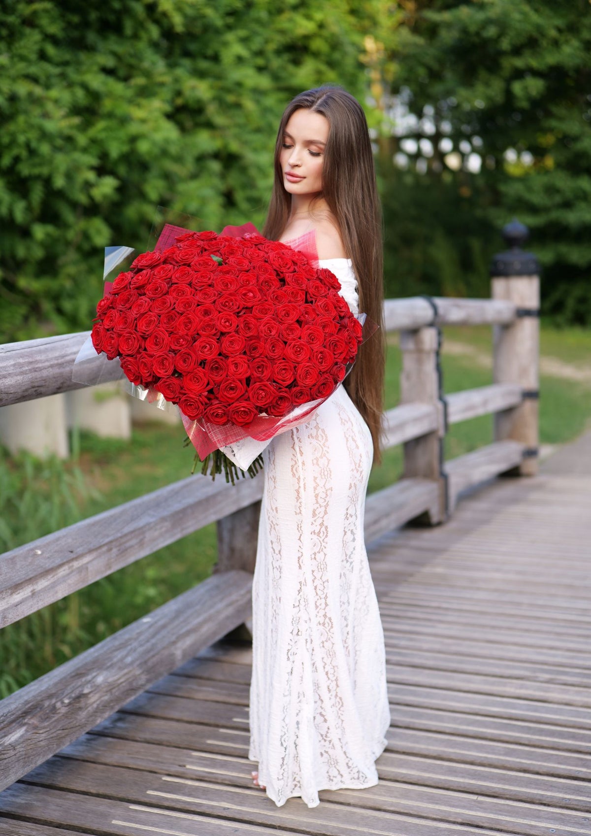 Diana in een witte jurk met een groot boeket rode bloemen tijdens een branding fotoshoot